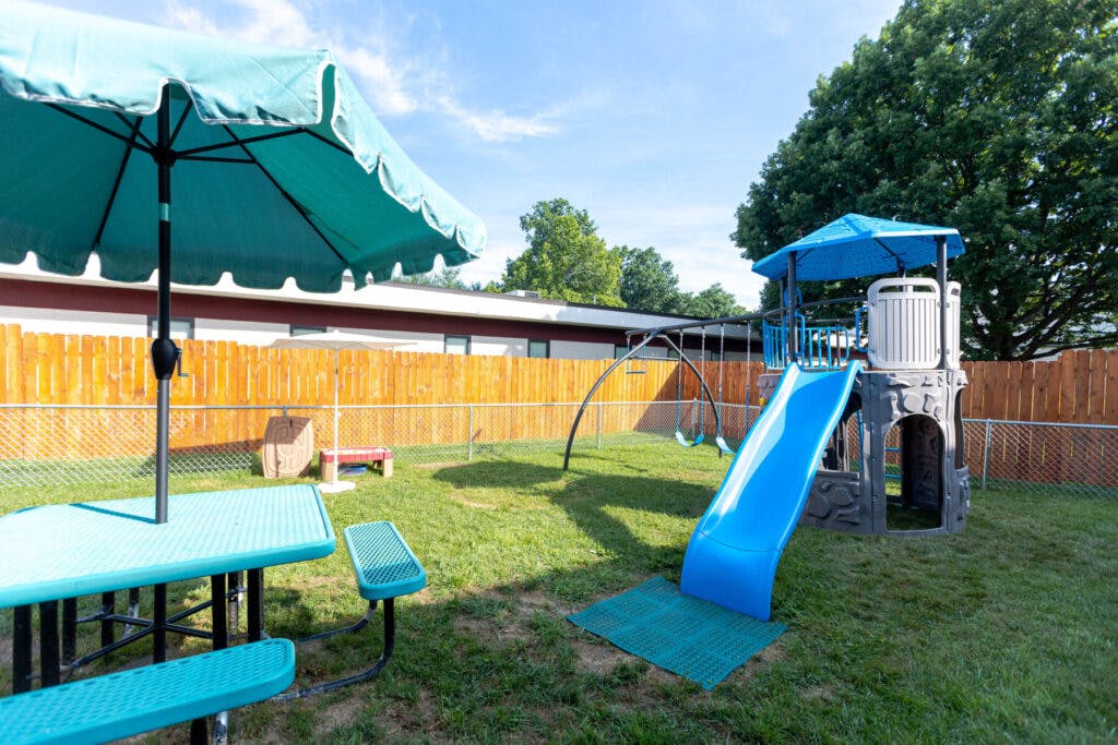 Playground with a blue slide, swings, and a picnic table with an umbrella