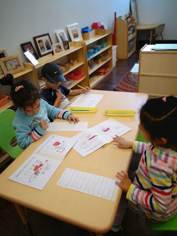Three children drawing and writing at a table in a classroom