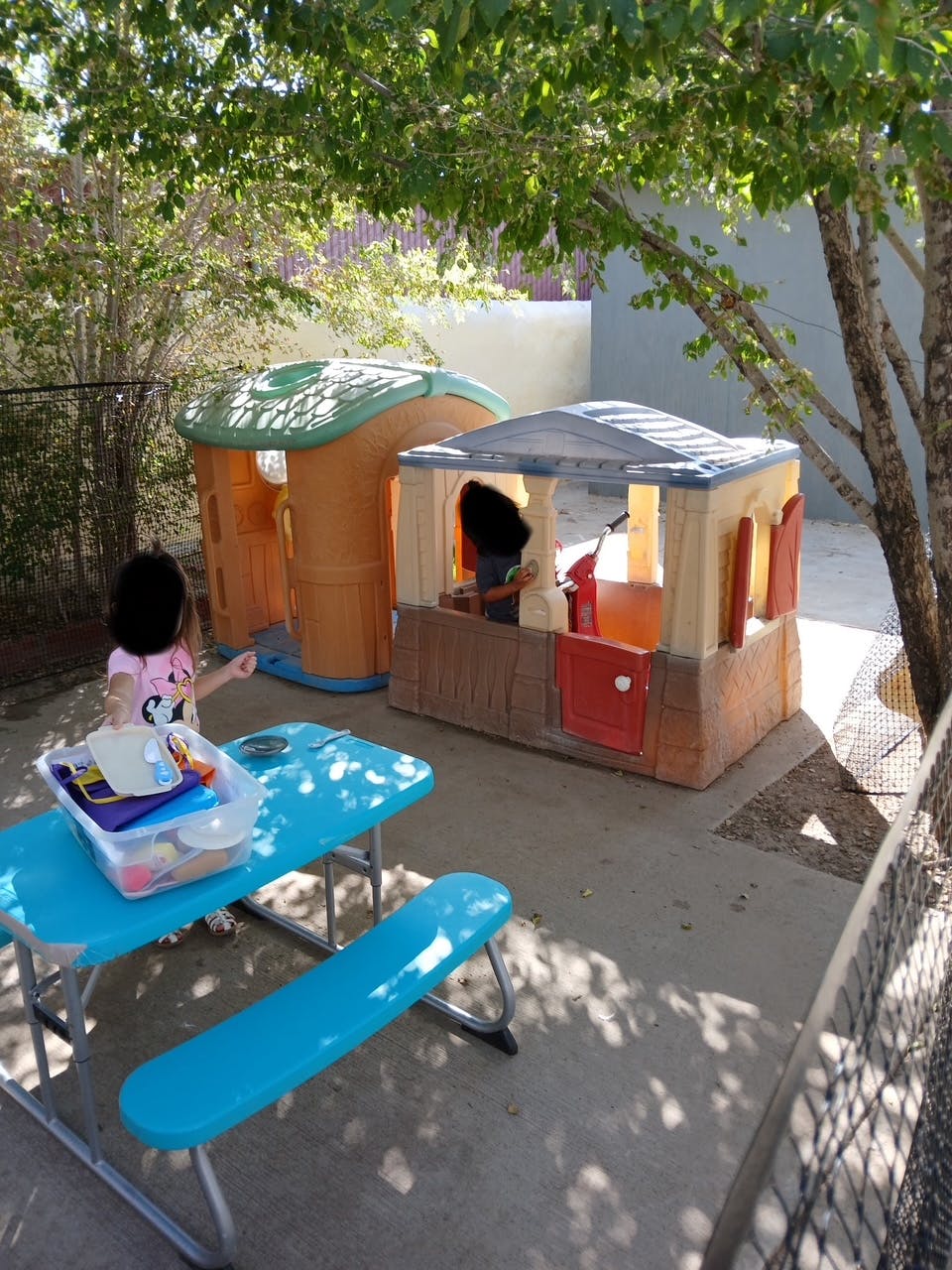 Child standing next to a blue picnic table with playhouses in the background
