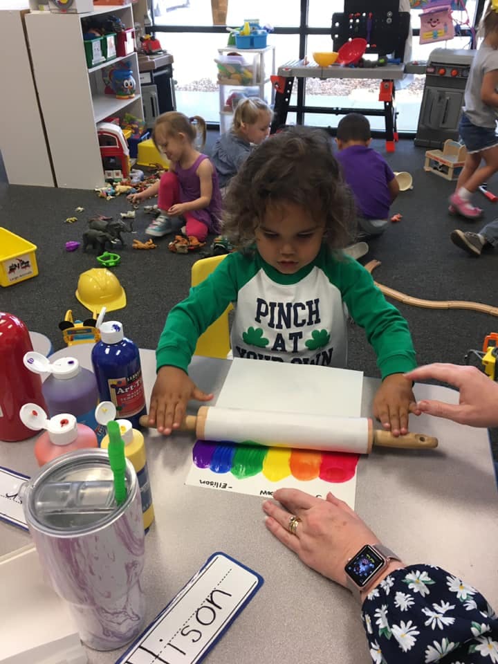 Child using a rolling pin to spread paint on paper