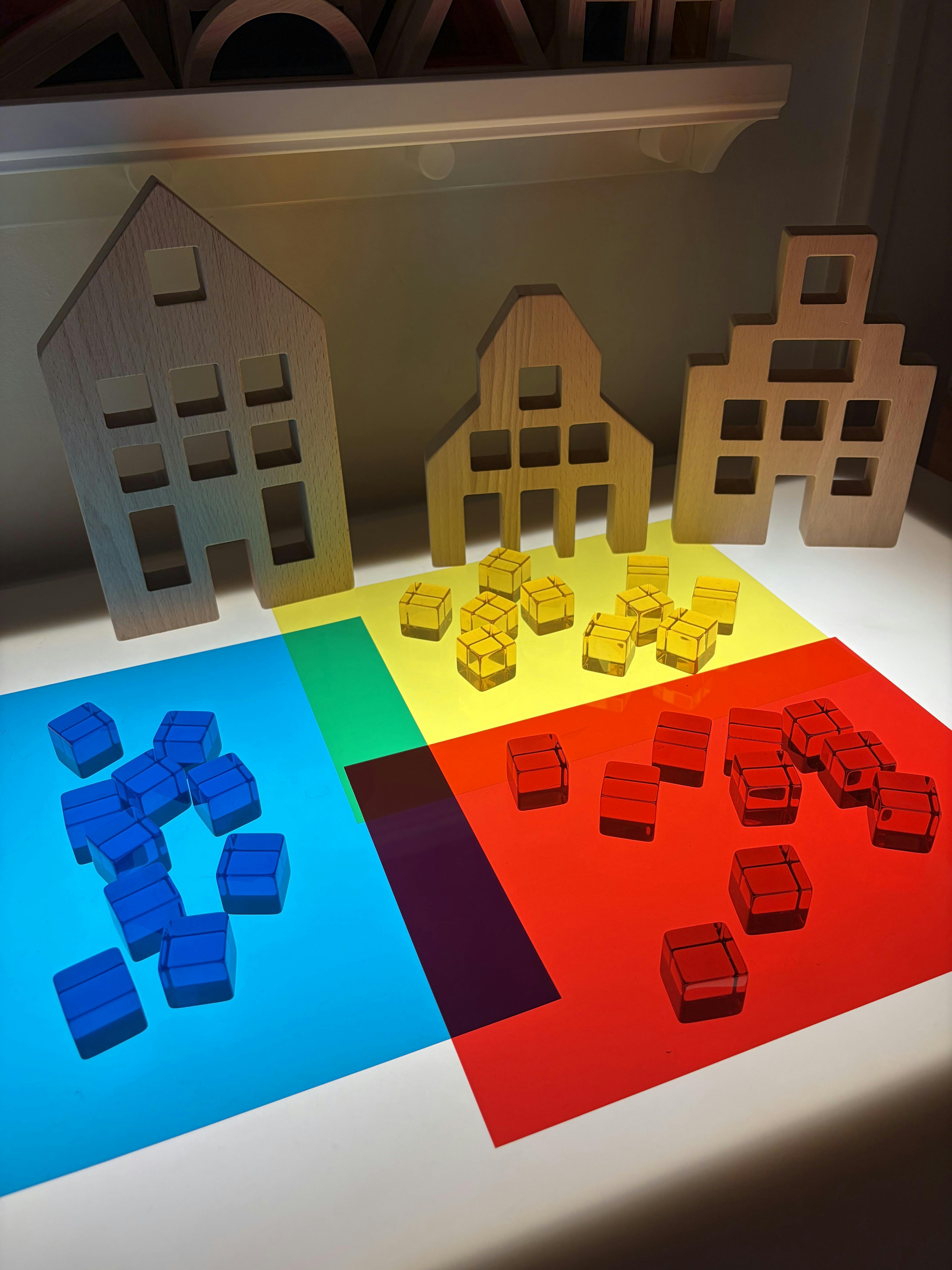 Wooden toy house frames arranged behind colorful transparent geometric blocks