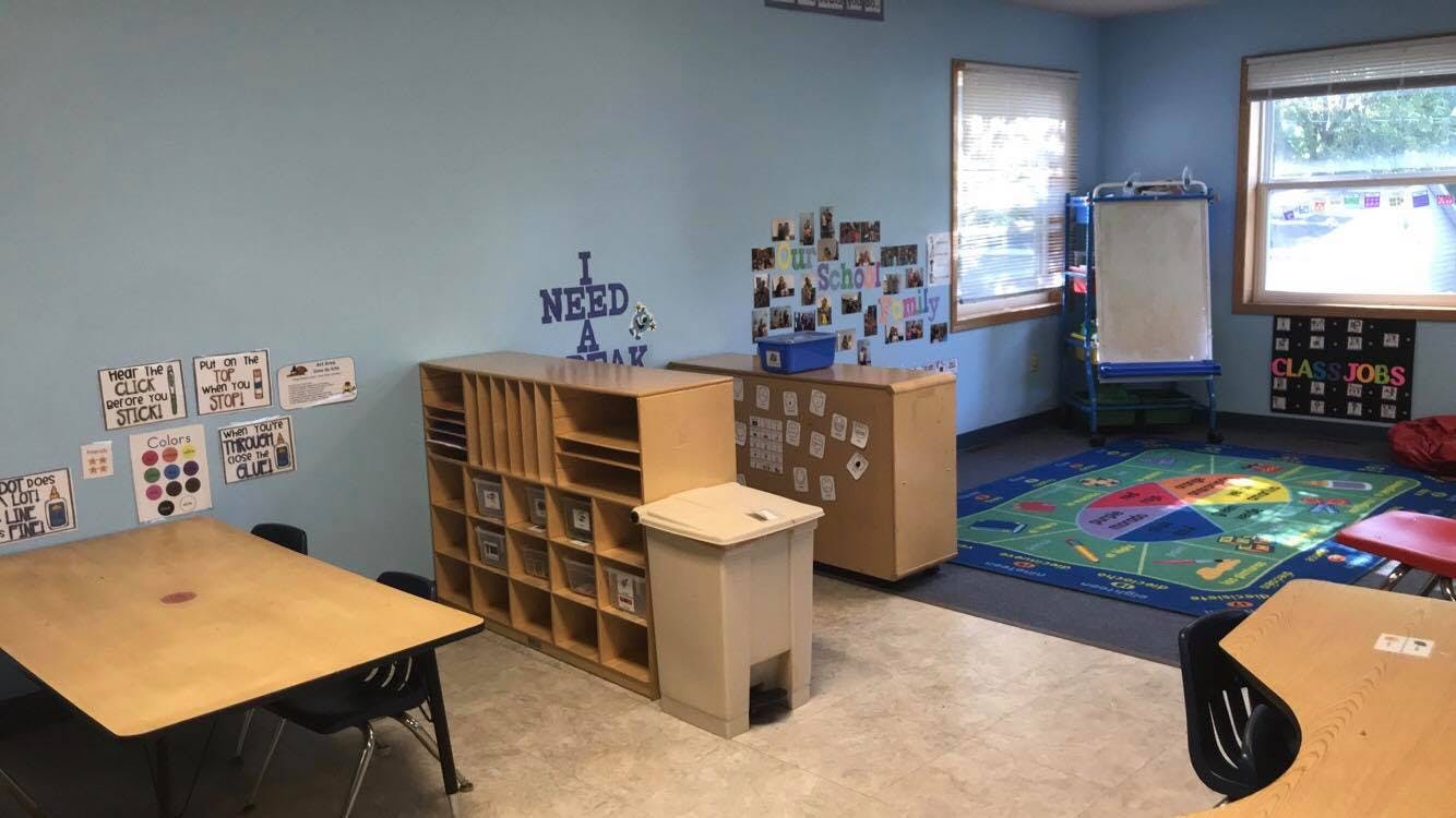 Classroom with tables, storage shelves, and a colorful rug