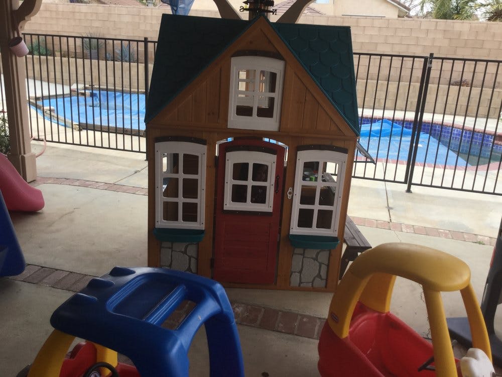 Playhouse with a red door and white windows next to a swimming pool
