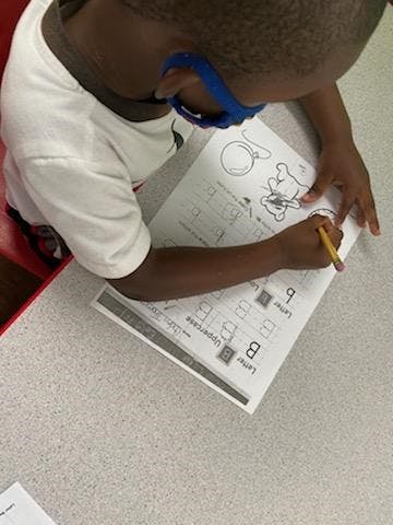 Child in blue glasses writing on a worksheet with a pencil