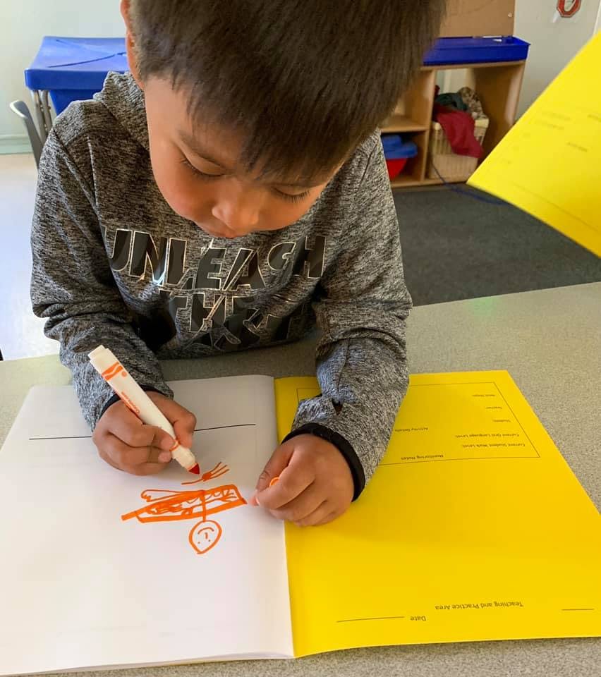 Child drawing with an orange marker in a notebook