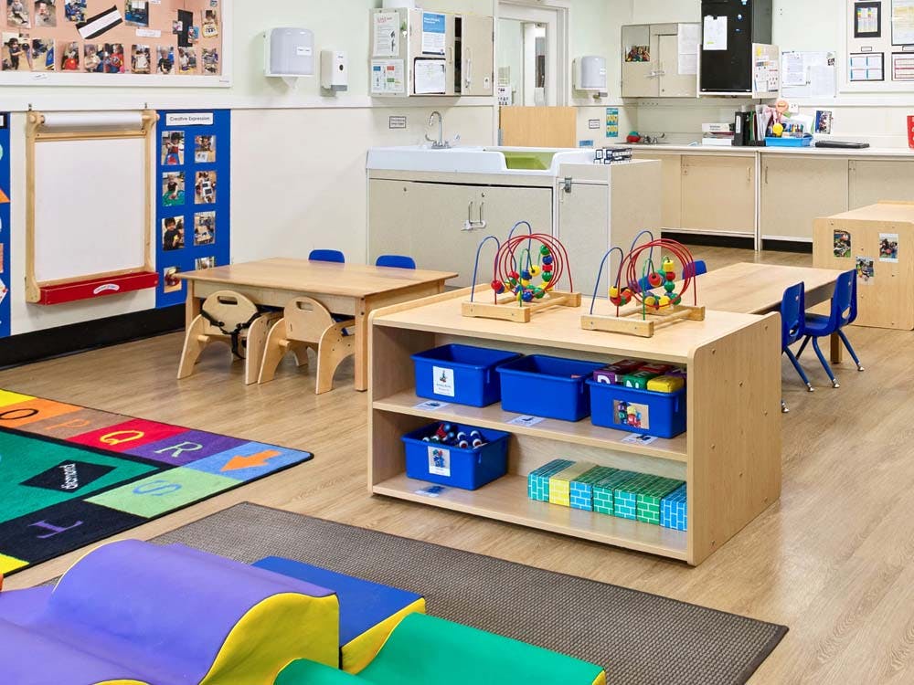 Classroom with tables, chairs, shelving with toys, and an alphabet rug