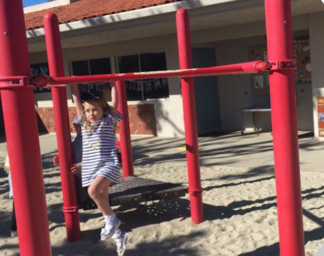 Child hanging from a red monkey bar on a playground