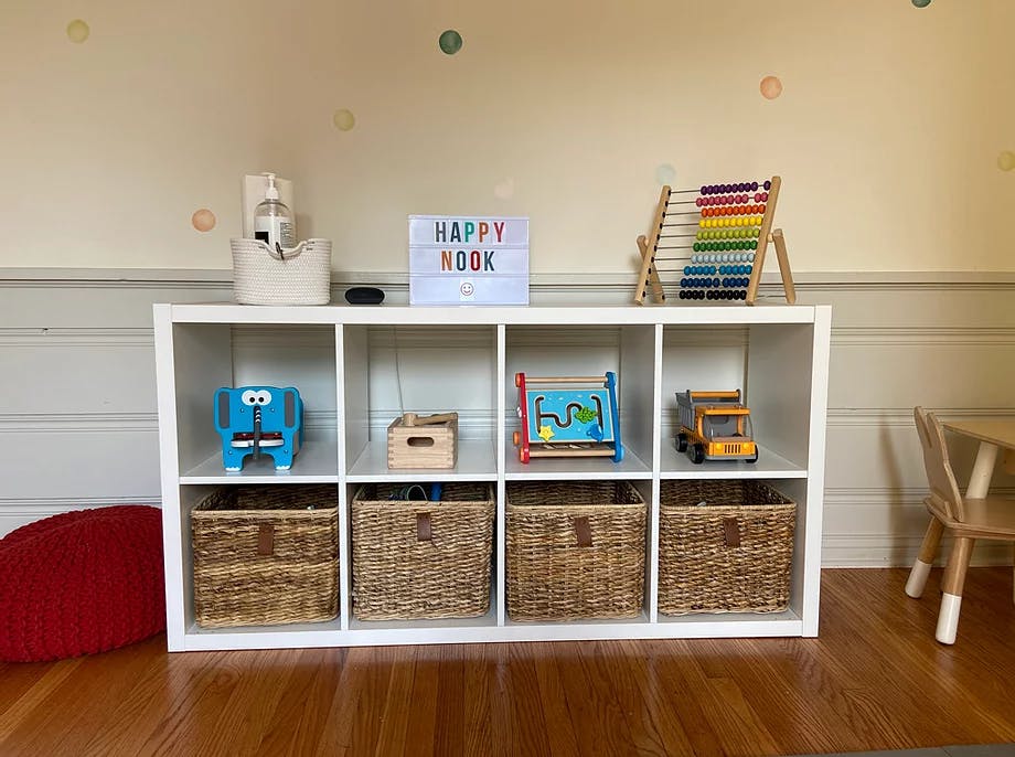 White storage shelf with toys and baskets, sign says "HAPPY NOOK"