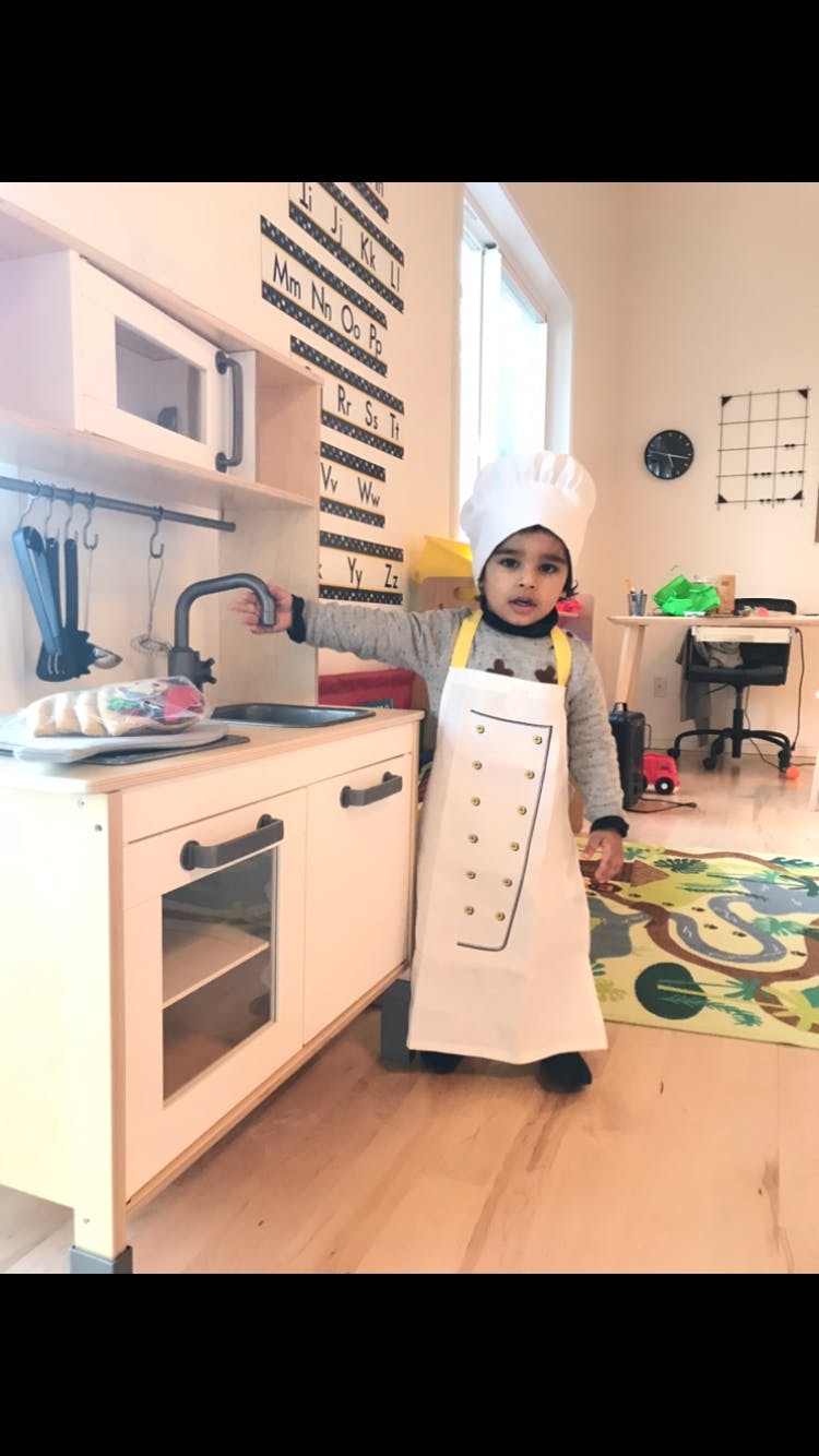 Child in chef's hat and apron at a play kitchen