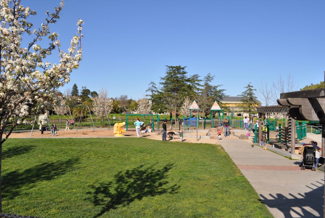 People and children playing in a park with playground equipment