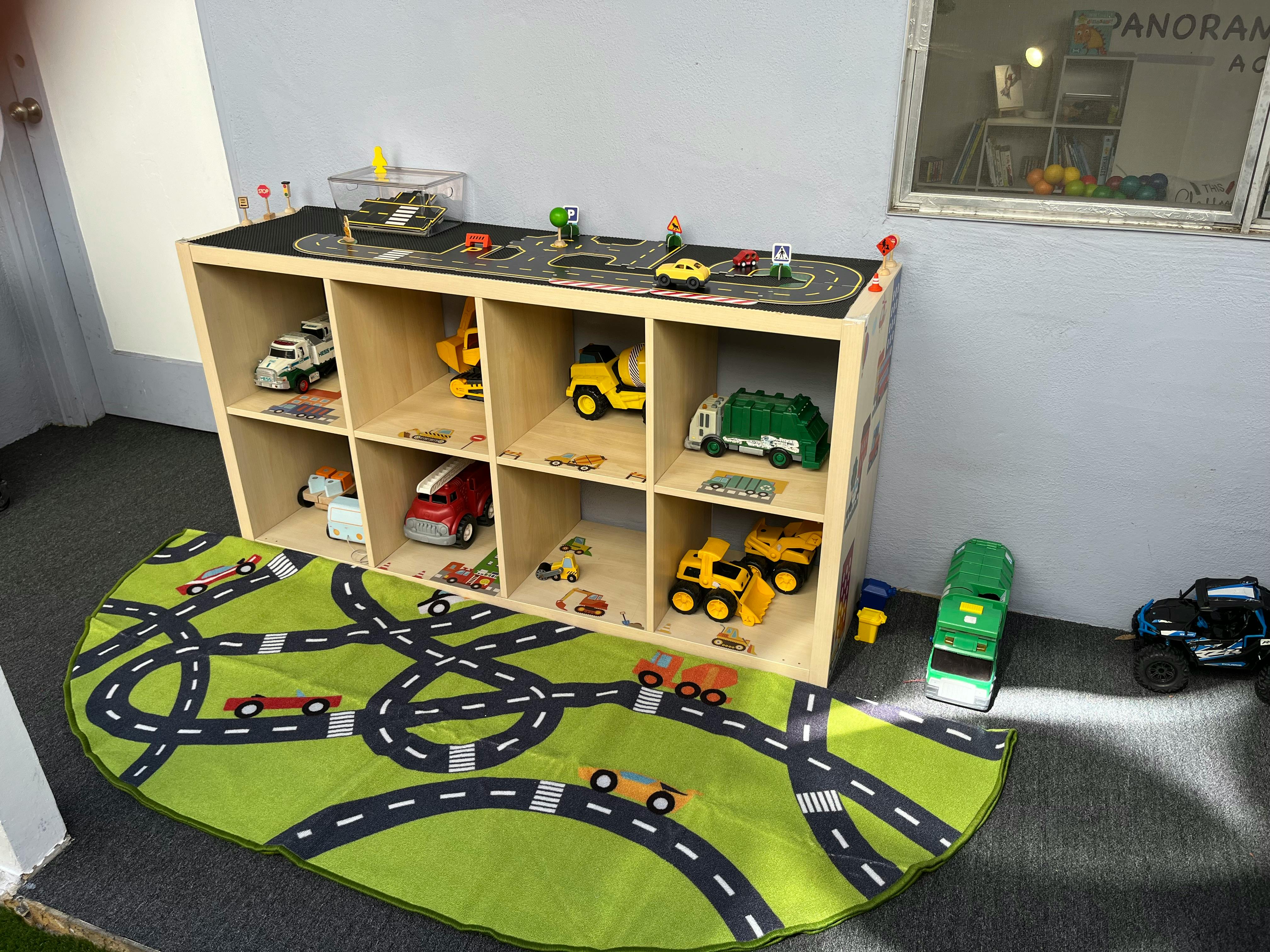 Toy cars on a road-patterned rug and in a cubby shelf