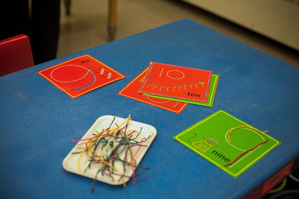 Cards with numbers and shapes on a blue table with a tray of colorful strings
