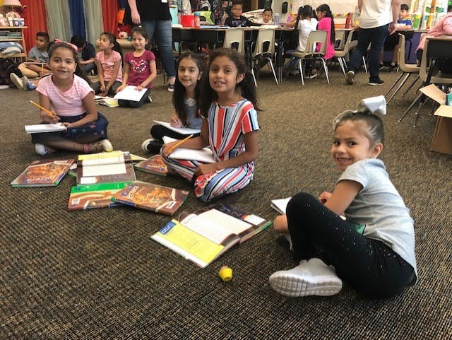 Children sitting on the floor with books and papers in a classroom
