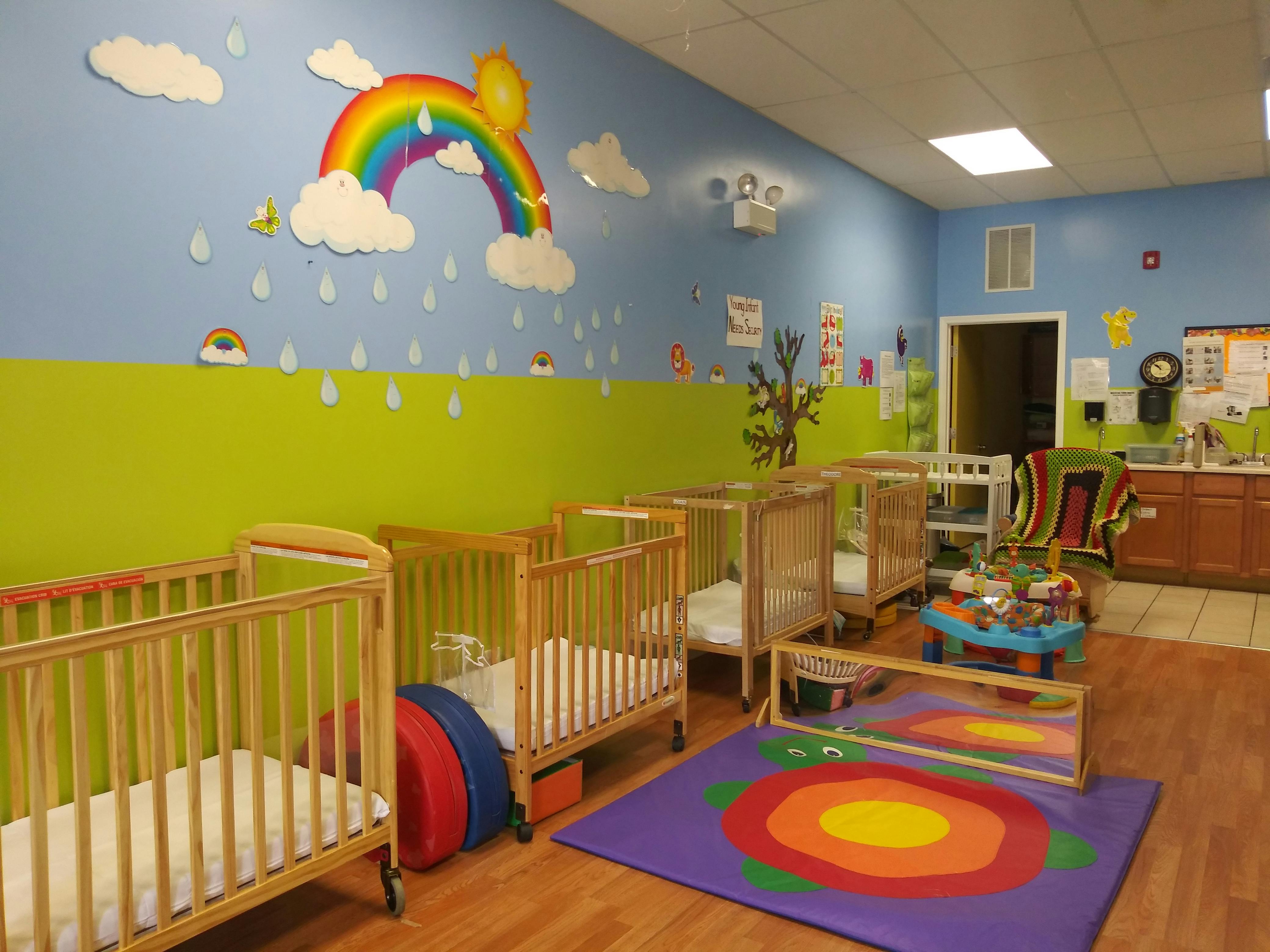 Nursery room with multiple cribs and a rainbow wall mural