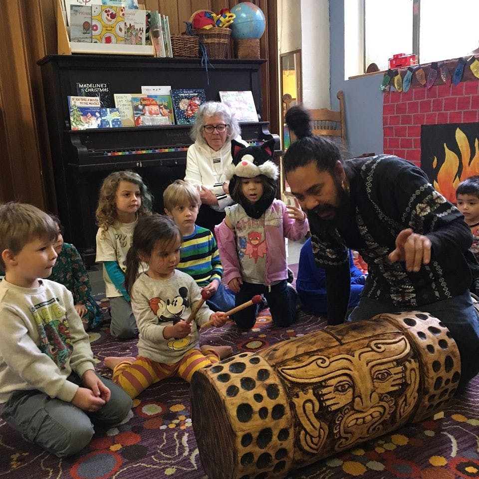 Adults and children gathered around a carved drum