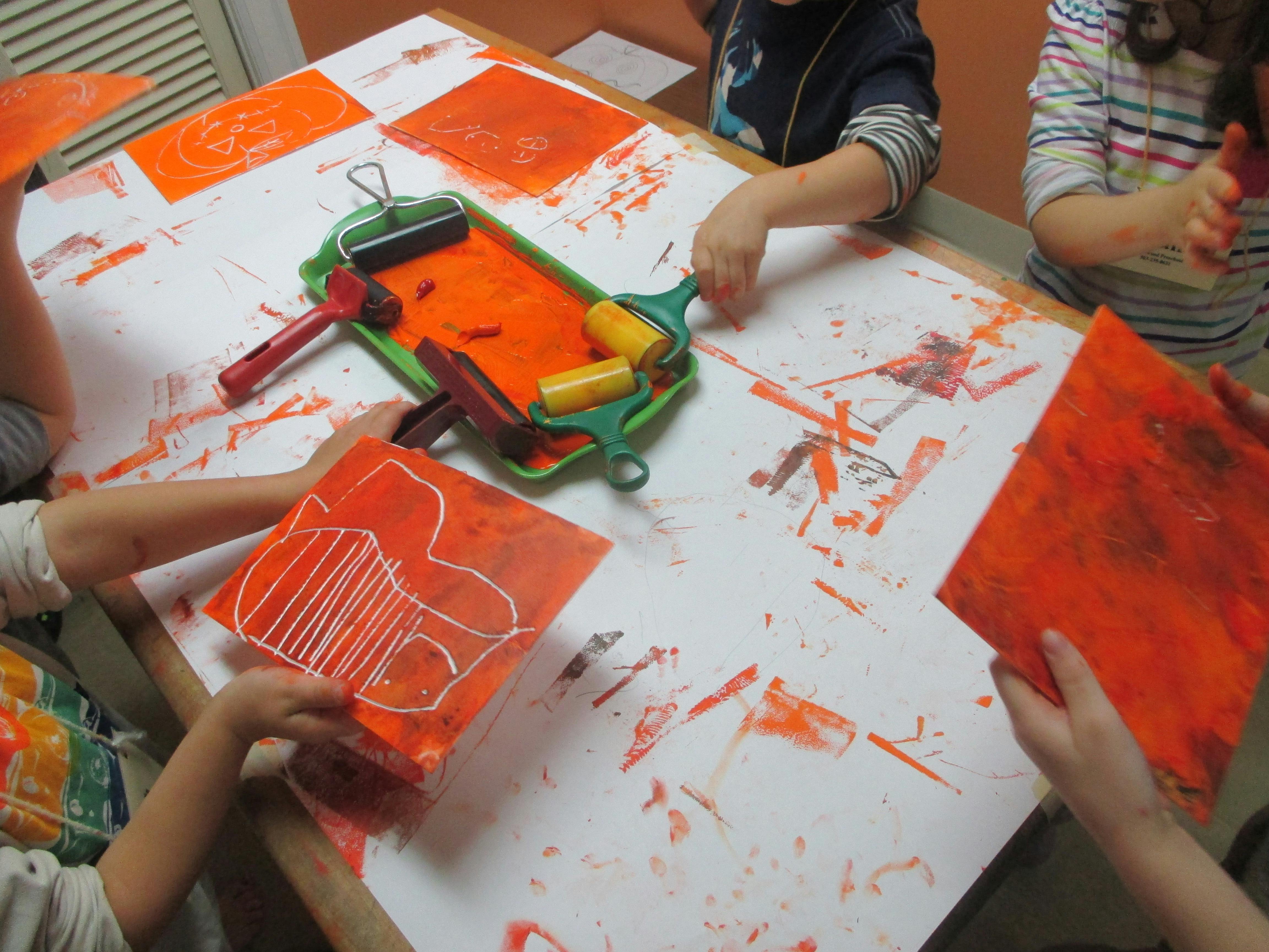 Children doing art with orange paint and rollers