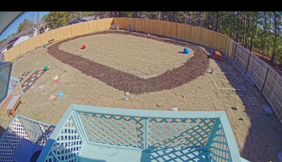 Overhead view of a fenced backyard with a dirt path and scattered objects