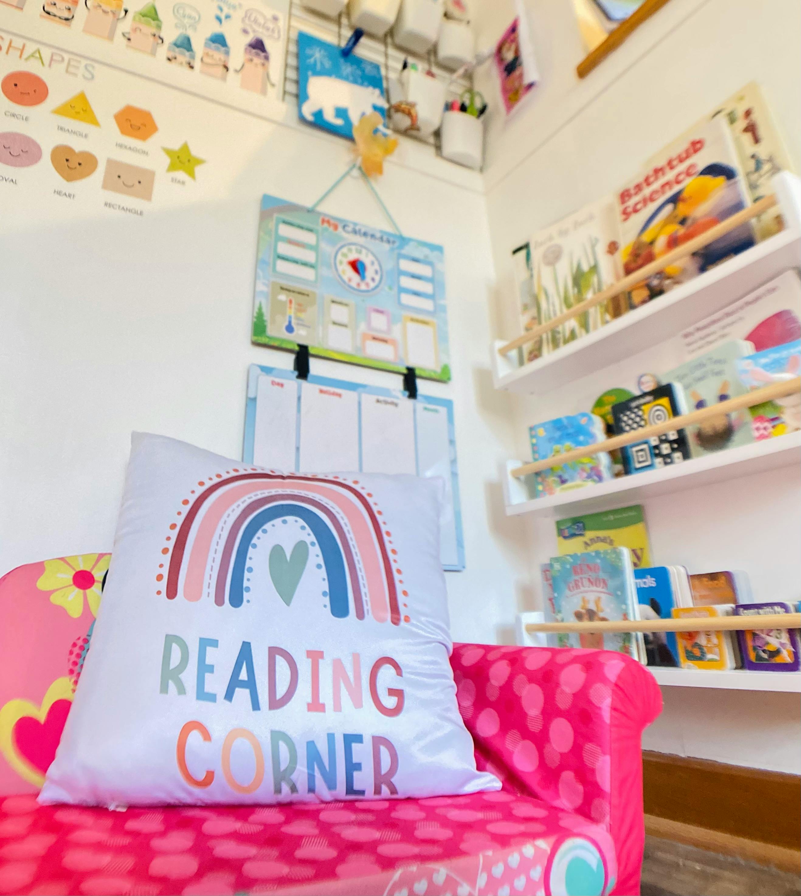 A pink child's armchair with a rainbow reading corner pillow