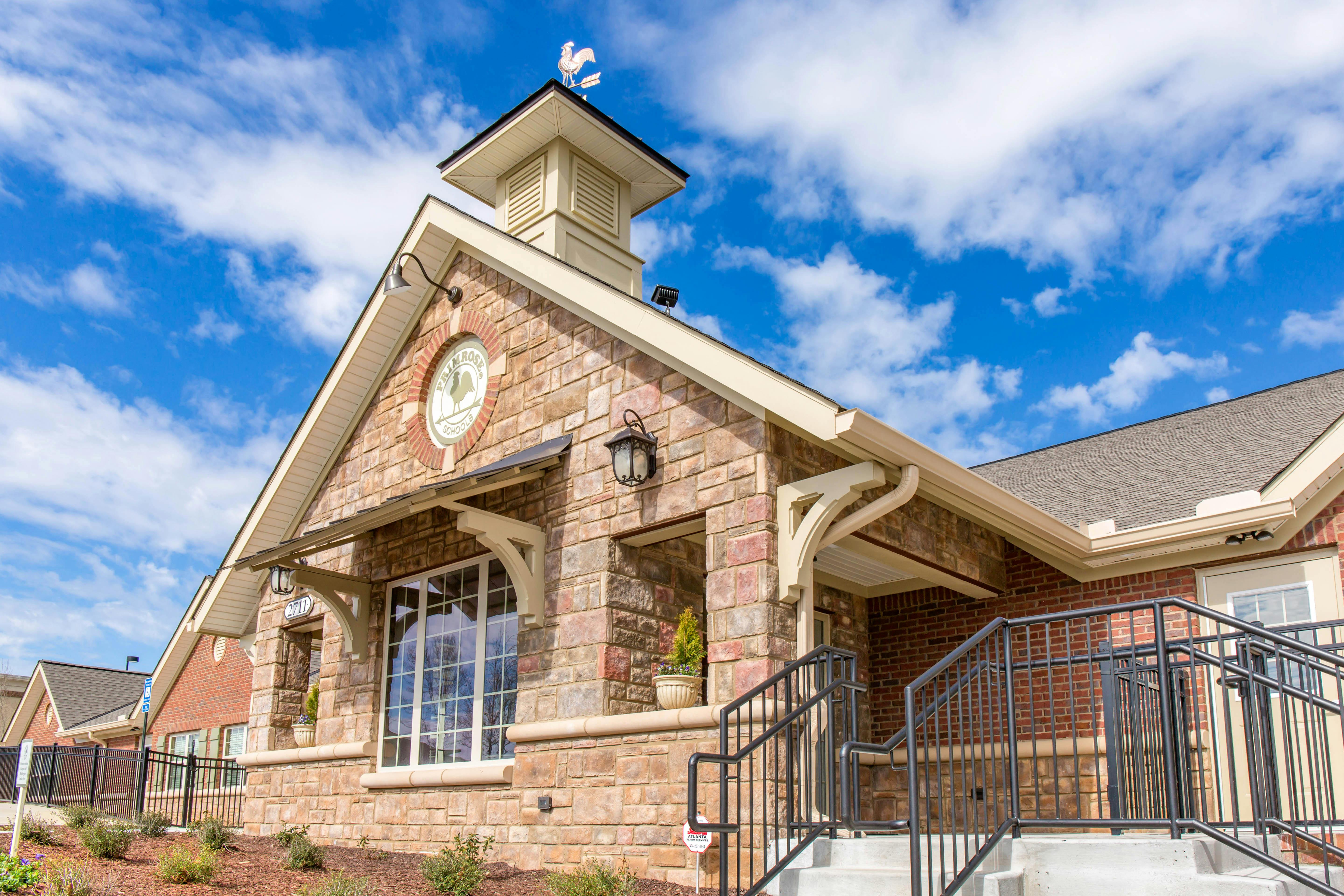 Brick building with a stone facade, tall cupola with a weathervane, and concrete steps
