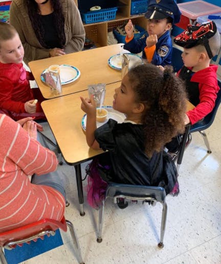 Children and an adult sitting at small tables in a classroom