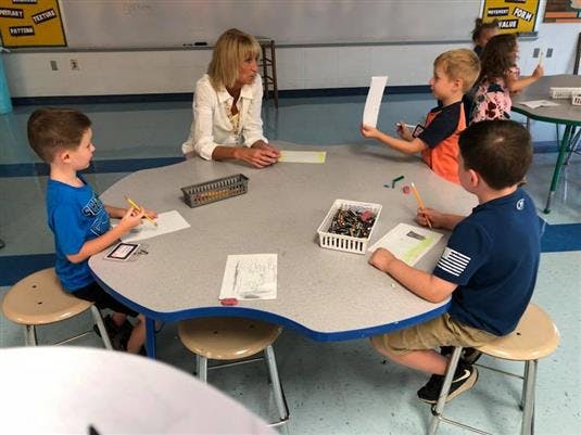 Adult and three children sitting at a table in a classroom