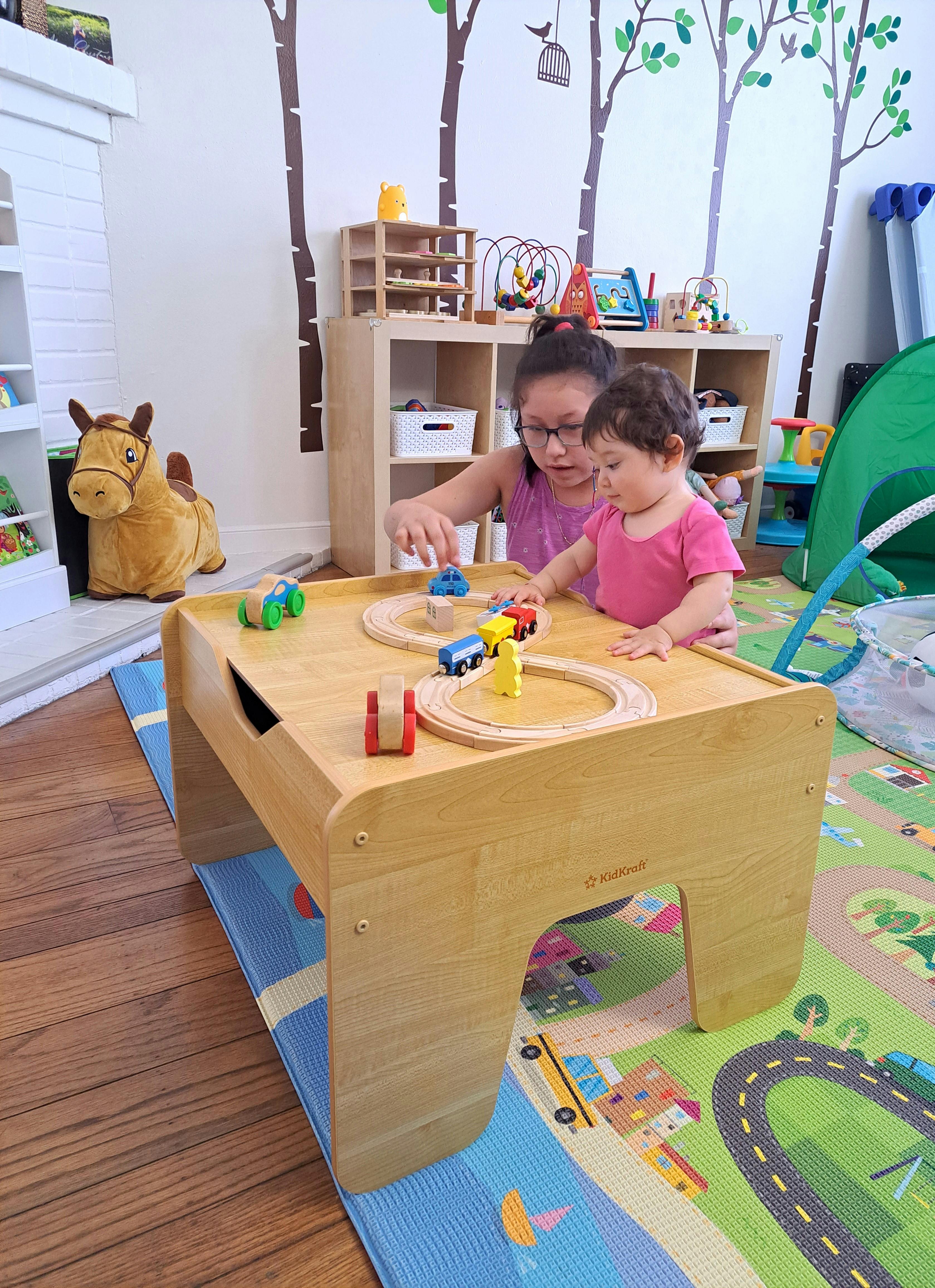 Two children playing with a toy train set on a wooden table