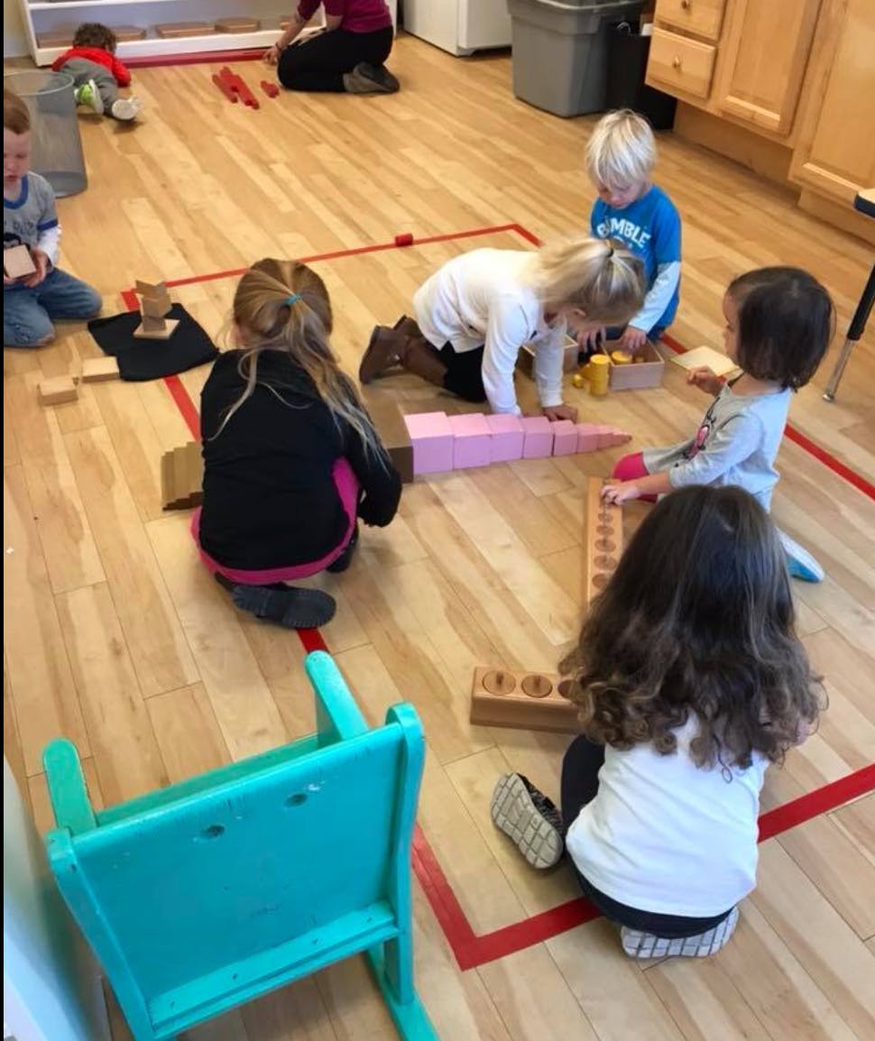Children playing with blocks on a wooden floor in a classroom