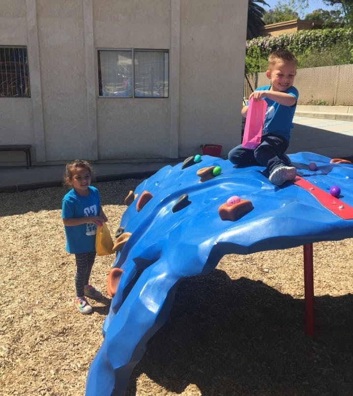 Child sitting on a blue climbing structure, another child standing nearby