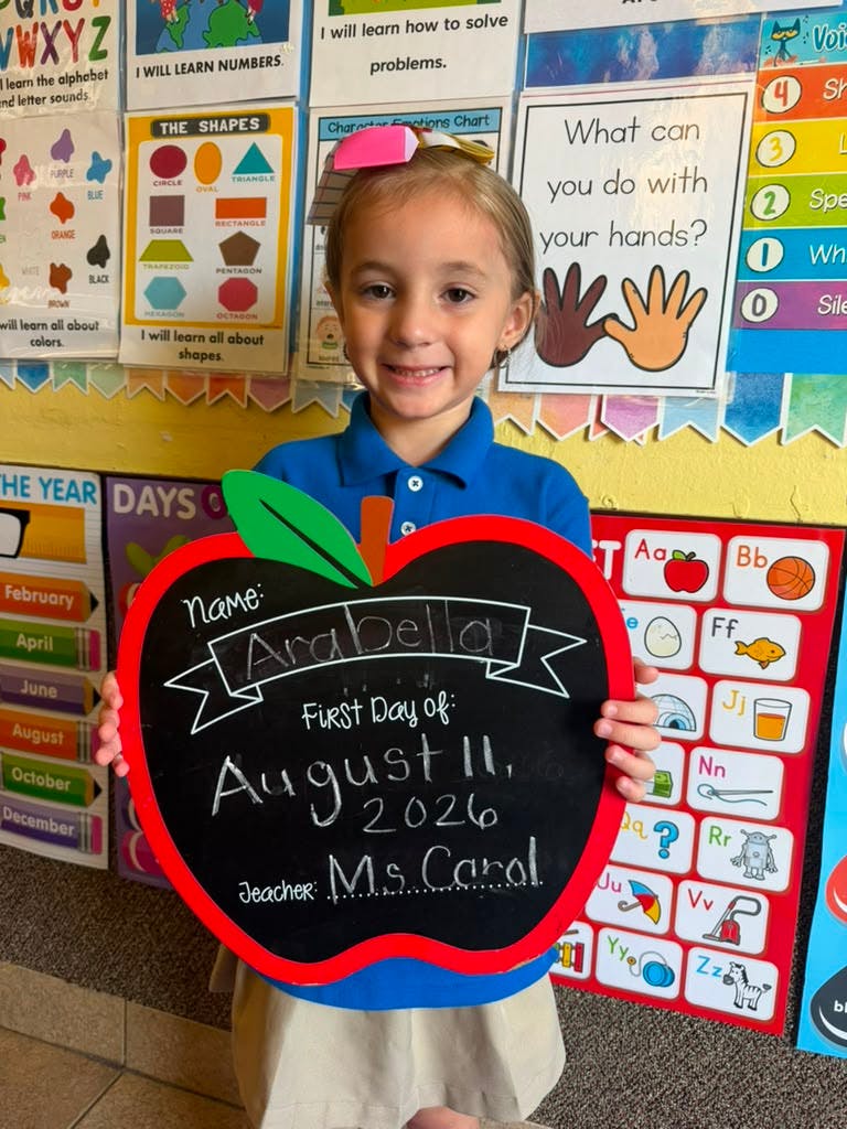 Child holding an apple shaped sign with school information in a classroom