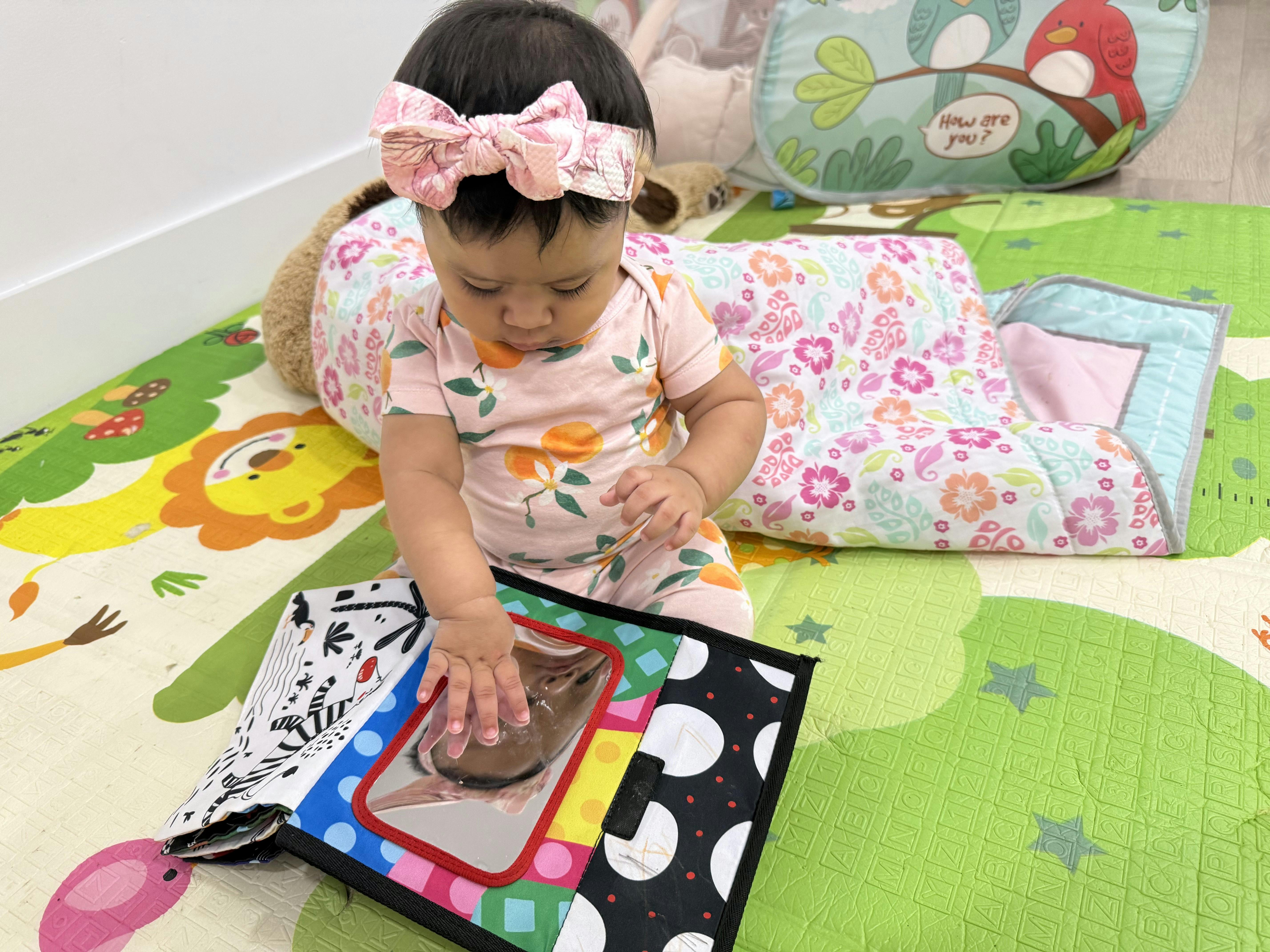 Child sitting on a play mat and touching a toy mirror