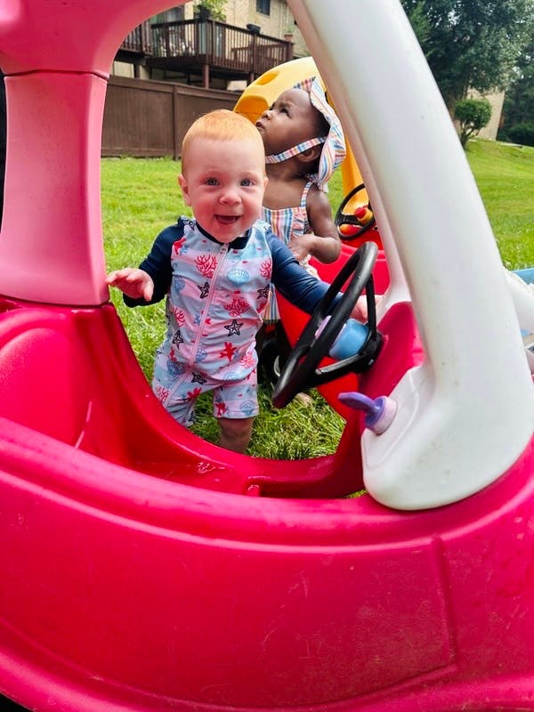 Two children playing in toy cars outdoors