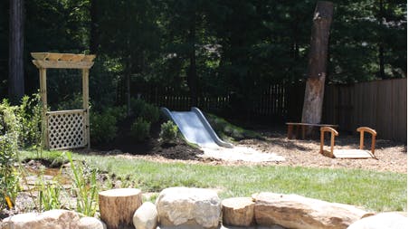 Outdoor play area with slide, wooden archway, and tree stumps