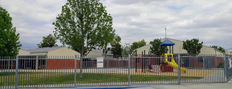 Playground with yellow slide and blue roof behind a fence