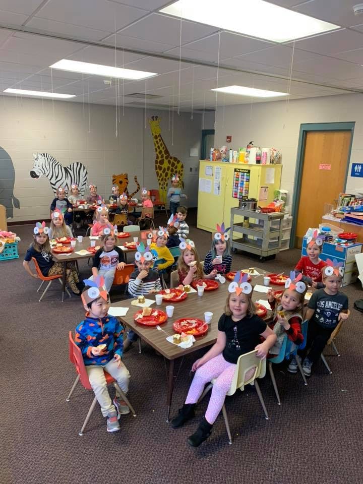 Children wearing animal headbands sitting at tables in a classroom