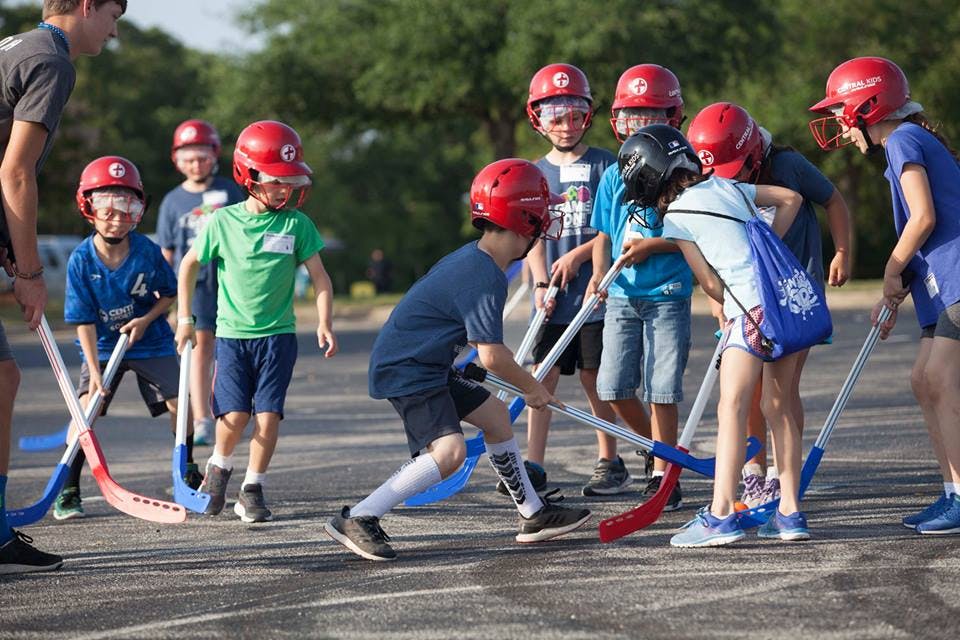 Children in helmets playing street hockey with sticks