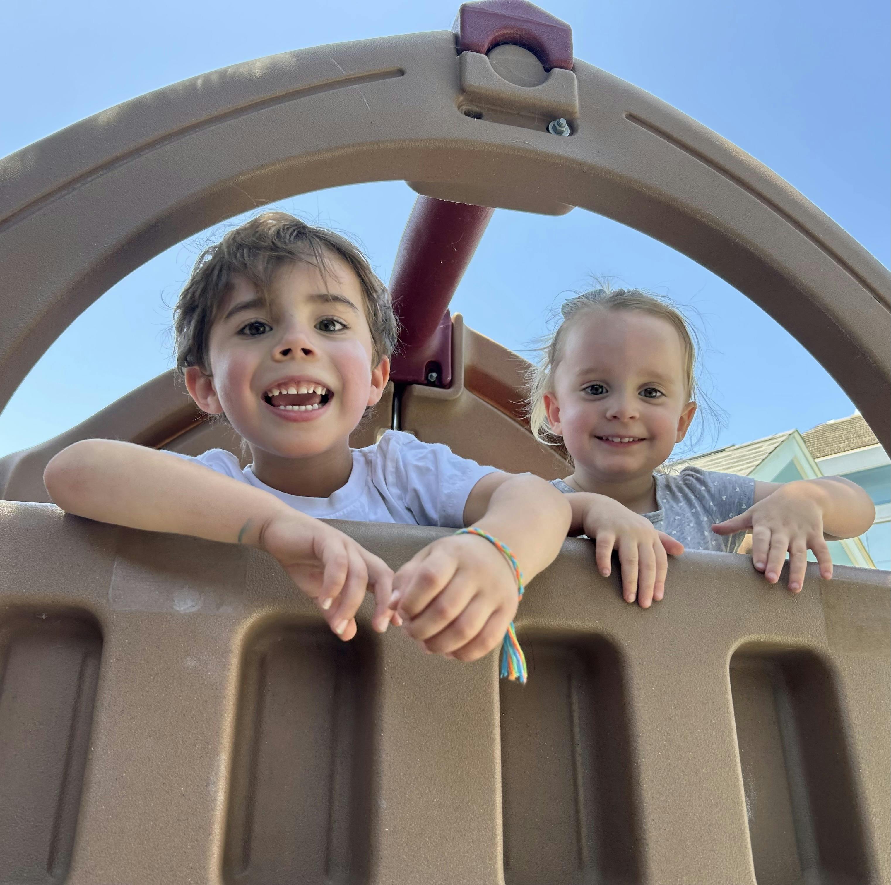 Two children looking over the top of a playground structure