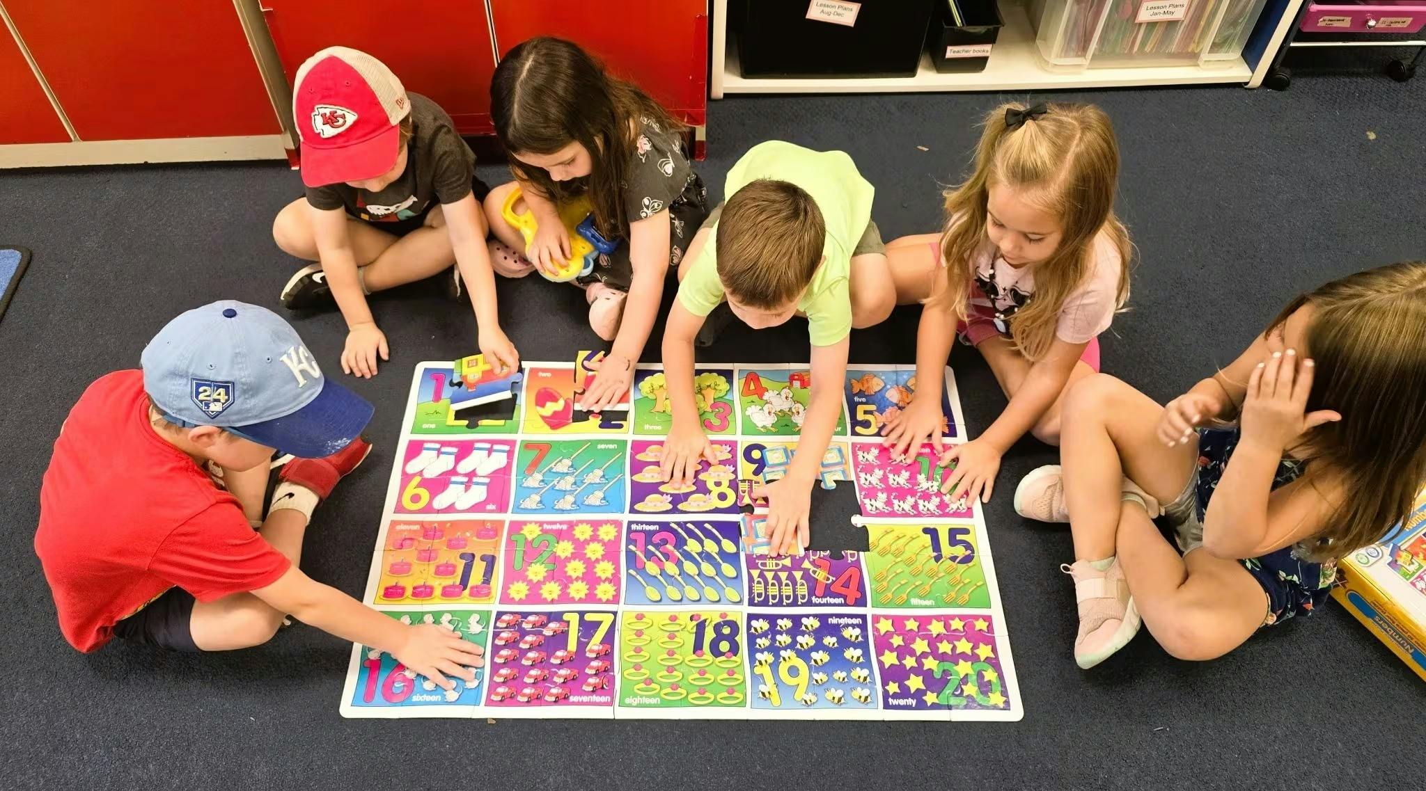 Five children on the floor working on a large number puzzle