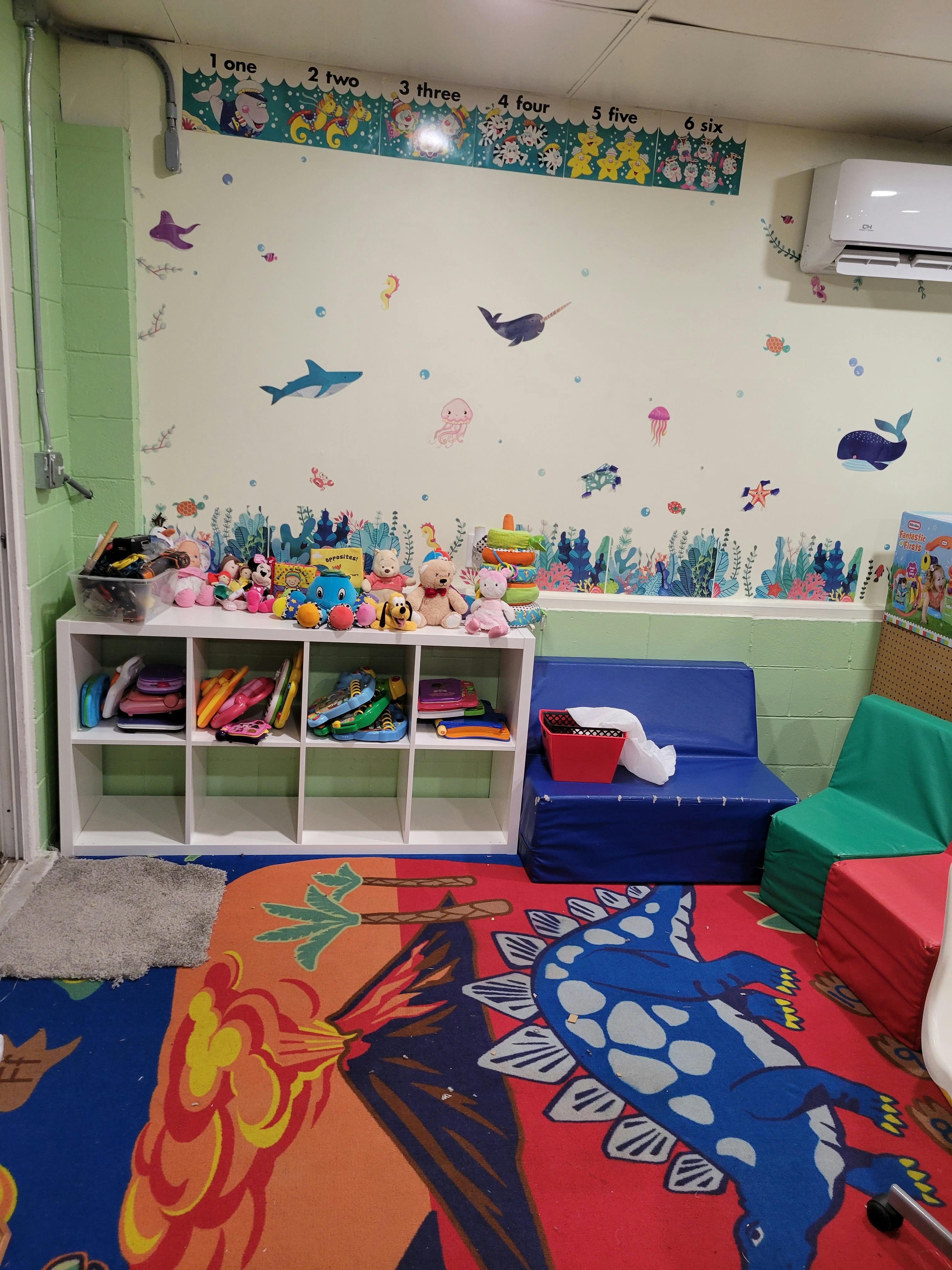 Playroom with colorful rug, toy shelf, and wall decals