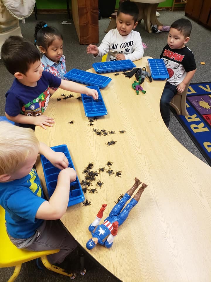 Children playing with ice cube trays and toy spiders at a table