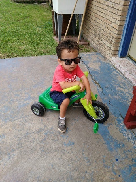 Child wearing sunglasses sitting on a green tricycle