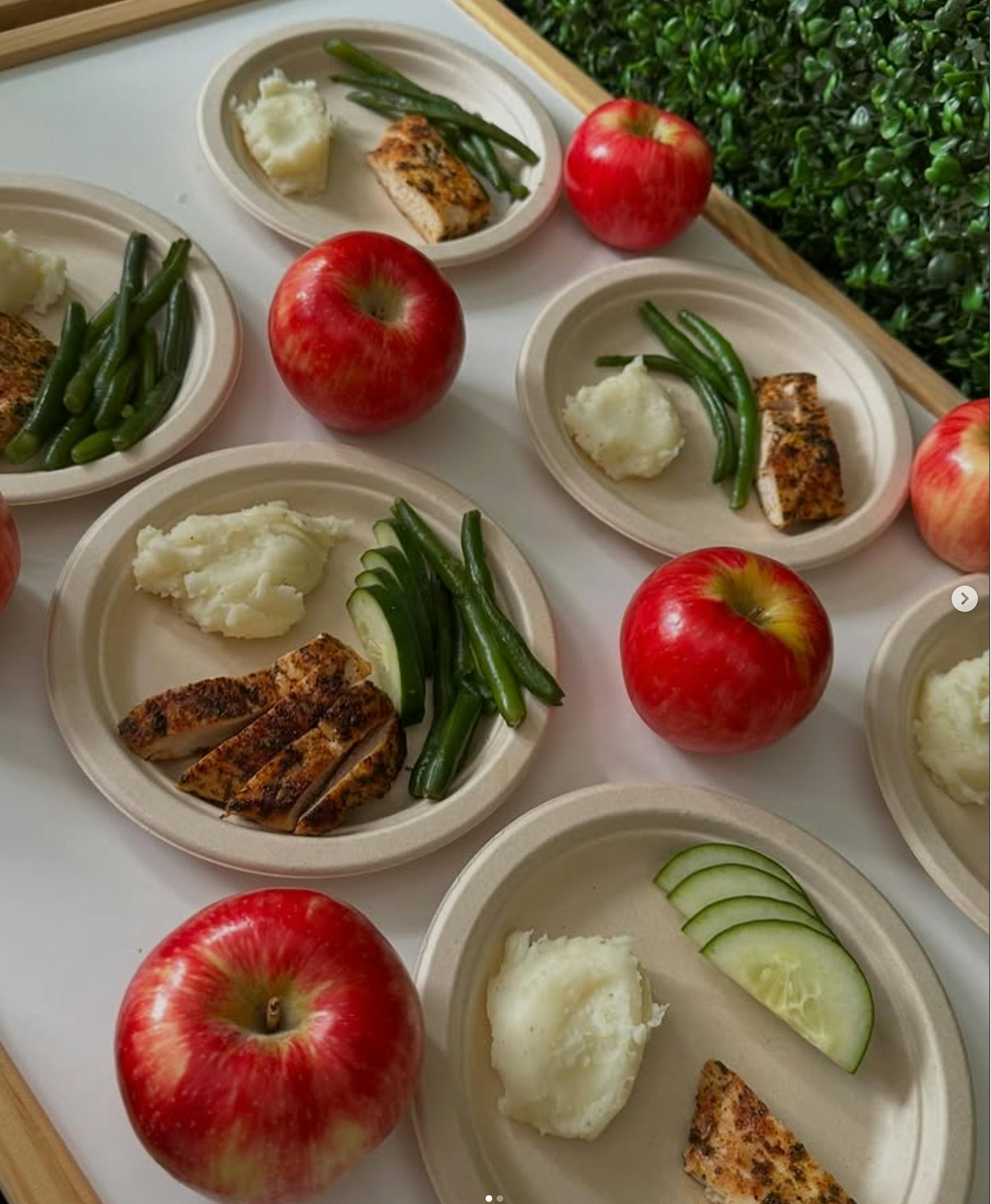 Multiple paper plates served with chicken, mashed potatoes, and green vegetables