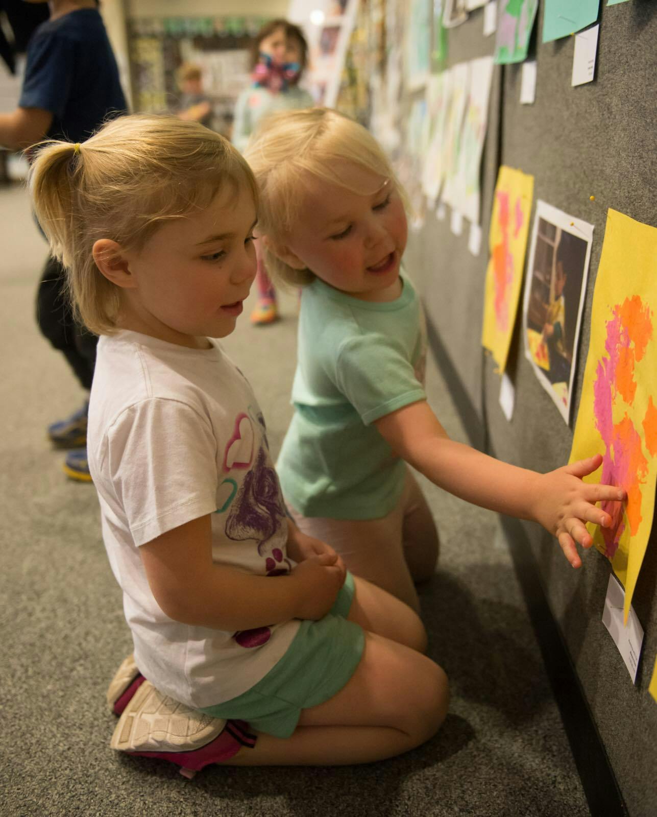 Two children kneeling and looking at artwork on a wall