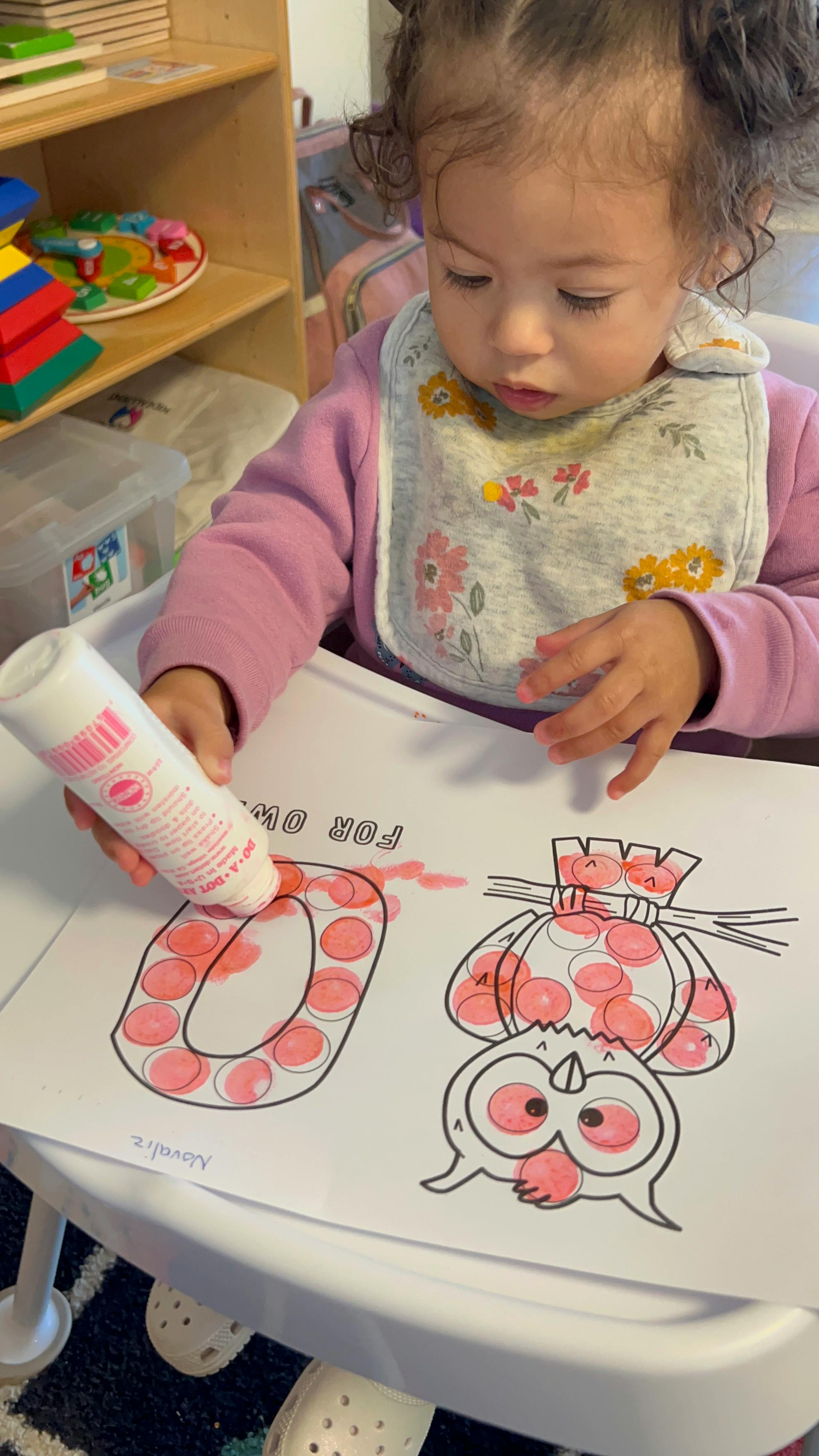 Child using a pink dot marker on a coloring page with an owl and letter O
