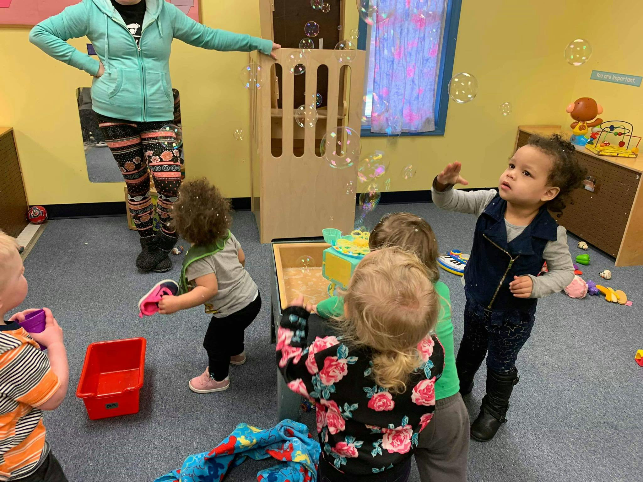 Person standing near children playing with bubbles in a classroom