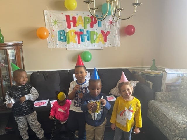 Four children wearing party hats in front of a Happy Birthday banner