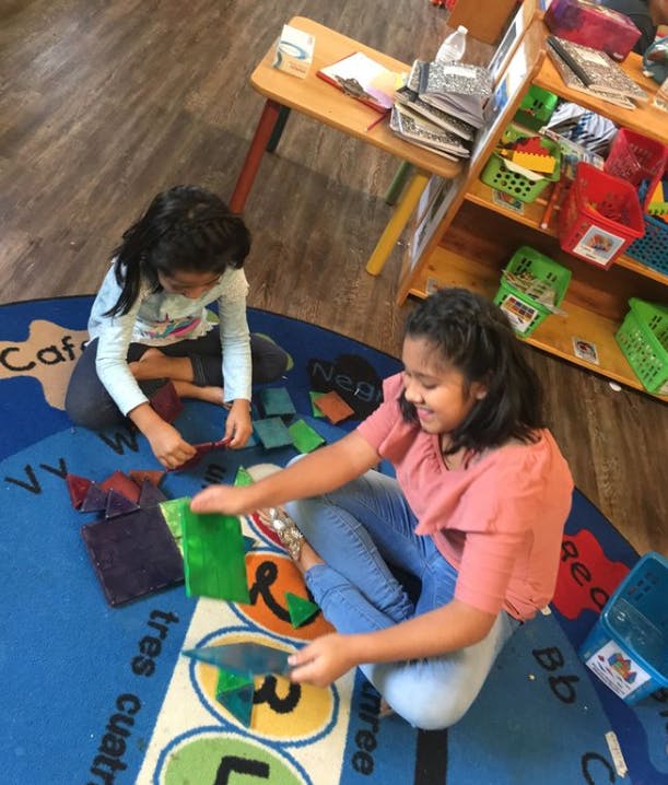 Two children sitting on a rug playing with fabric squares