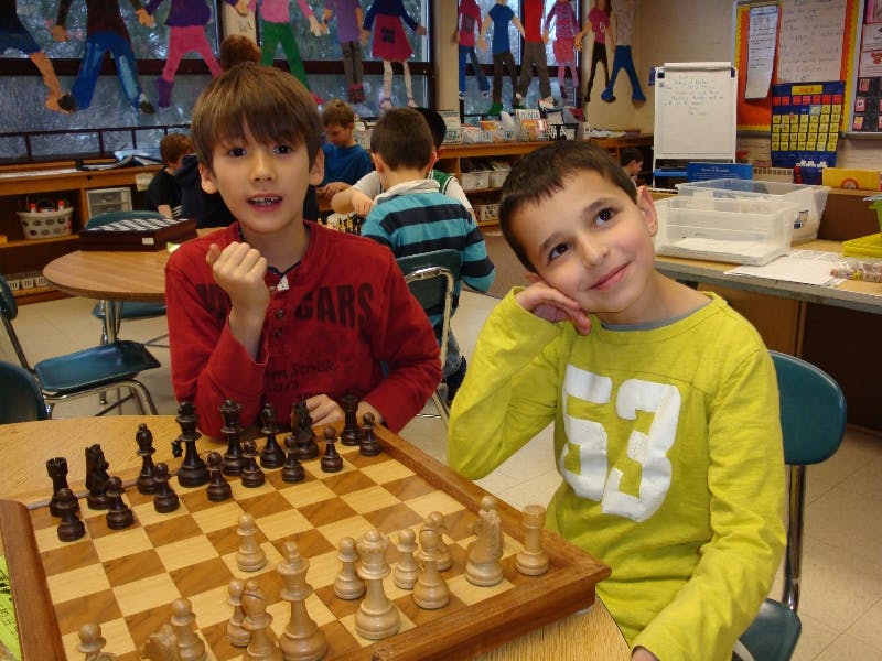 Two children sitting at a table with a chessboard