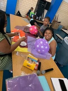 Adult and children at a table with craft supplies and balloons