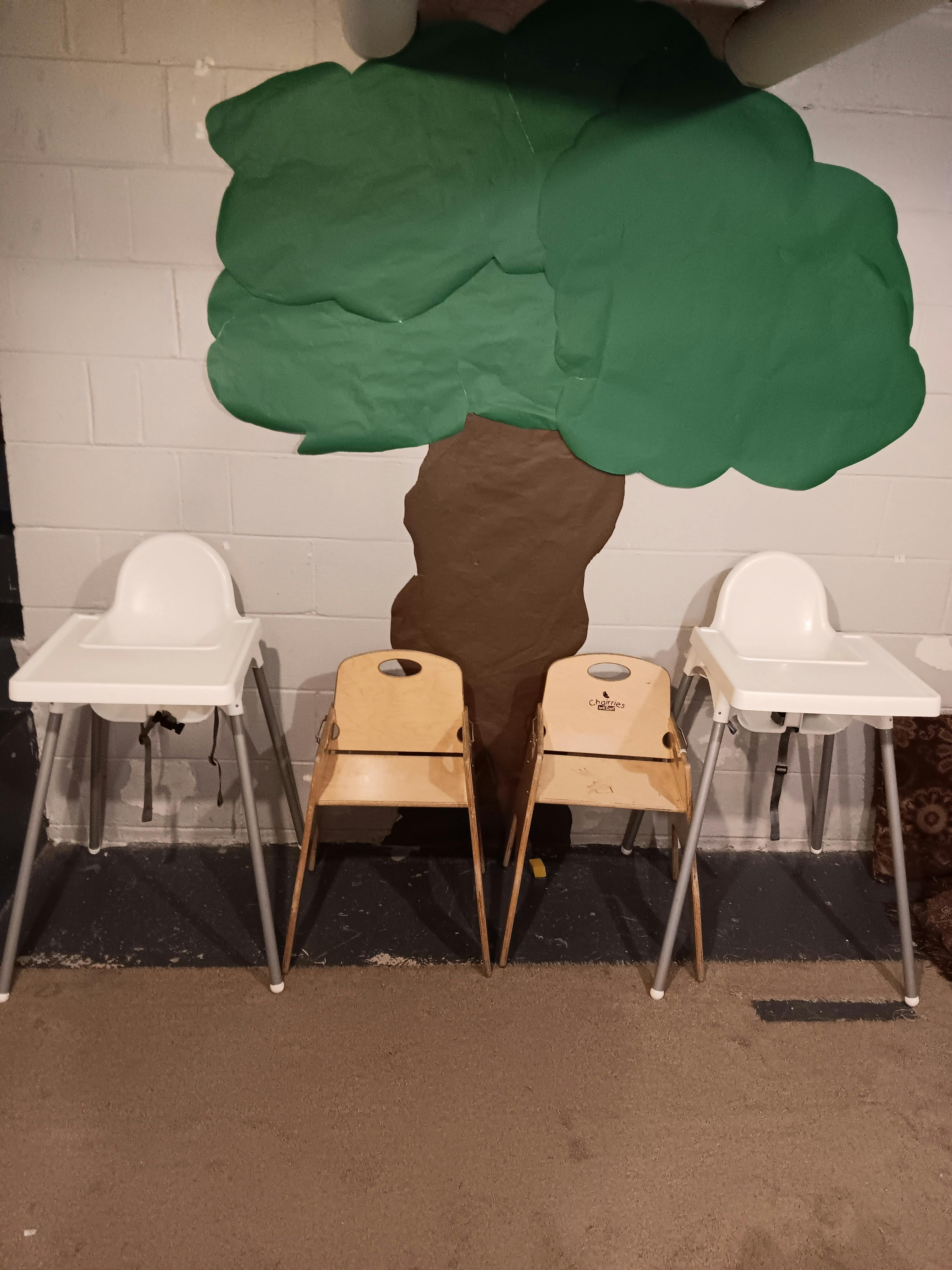 Two high chairs and two wooden chairs under a painted tree on a wall