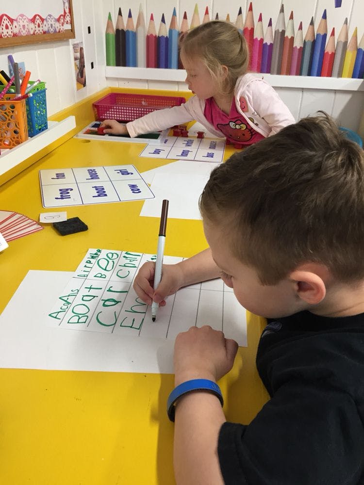 Child writing on paper with a marker, another child in background